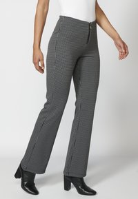 Črno-bele houndstooth hlače s ravnimi nogavicami, visokim pasom, zadrgo in obutevjo z visokimi petami v črni barvi.