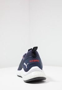Navy sportovní boty s texturovaným síťovým svrškem, červeným detailem "HYBRID", černou trakční podrážkou a polstrovanou bílou mezipodrážkou. Součástí je i poutko na patě.