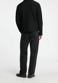 Chaqueta negra de manga larga, ajuste casual. Combinada con pantalones vaqueros oscuros y holgados y zapatos negros. Diseño simple, sin patrones ni detalles visibles.