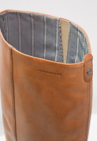 Bottine en cuir marron avec une texture lisse, dotée d'une doublure en tissu rayé et d'un accent métallique de marque sur le côté.