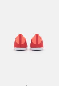 Røde atletiske sko med et textured design, der har en glat hæl og kontrasterende hvide såler, set fra bagsiden.