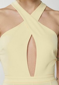 Top sin mangas amarillo con un diseño entrecruzado en el escote y un corte en forma de llave. Textura suave, tela blanda, hardware mínimo.
