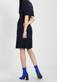 Mörkblå klänning med korta ärmar och dragkedjedetalj bak; ihop med blå ankelstövlar med blockklackar.