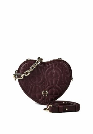 Sac à main en forme de cœur bordeaux foncé avec motif matelassé, détail chaîne dorée, fermeture éclair et bandoulière assortie amovible placée à côté.