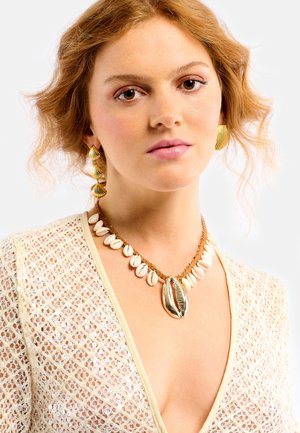 Boucles d'oreilles en forme de coquillage couleur or et collier tressé avec des coquillages blancs et un pendentif central en coquillage. Le haut présente un design texturé couleur fauve.