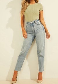 Lys grøn ribbet kortærmet top sat i kombination med højtaljede, slidte lyseblå jeans. Modellen har nude højhælede sko på.