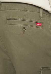 Pantalones cargo de algodón verde oliva con un bolsillo trasero, que cuentan con un cierre de botón y una pequeña etiqueta roja de Levi's en el lateral. Textura suave.