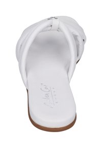 White flat sandal with a smooth leather upper featuring twisted straps, an open toe, and a brown rubber sole. Elegant and minimal design.