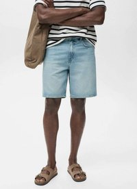 Șorturi din denim de culoare albastru deschis, cu o croială relaxată, purtate cu o cămașă în dungi și sandale maro, ținând o geantă bej. Textură netedă, tăietură până la genunchi.