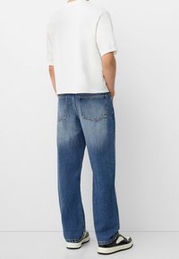 Valkoinen lyhyt t-paita, rento siniset farkut haalistuneella tekstuurilla ja mustavalkoiset tennarit. Farkkujen takataskut näkyvissä.