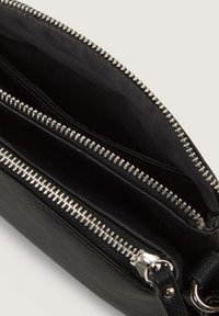 Schwarze Leder-Crossbody-Tasche mit drei Reißverschlussfächern, silbernem Beschlag und einem weichen Stofffutter. Texturierte Außenseite mit glatter Oberfläche.
