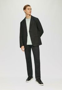 Czarna marynarka o luźnym kroju, zapinana na dwa guziki, z przednimi kieszeniami, w połączeniu z jasnoróżowym T-shirtem i ciemnymi spodniami, dopełniona czarnymi trampkami.