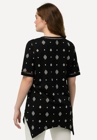 Túnica negra con patrones geométricos blancos, escote redondo, mangas cortas y dobladillo curvado. Fabricada en tela ligera.