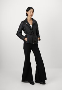 Black quilted jacket with a belted waist, long sleeves, and a high collar. The jacket features gold-tone hardware and a fitted design.