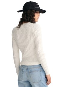 Weißer Strickpullover mit langen Ärmeln, gerippten Bündchen und rundem Halsausschnitt, kombiniert mit hochtaillierten hellblauen Jeans.