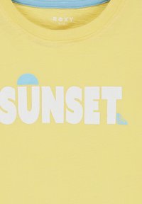 Žluté tričko s kulatým výstřihem, na kterém se nachází výrazný bílý nápis "SUNSET" a malý modrý akcent nad písmenem 'S'. Součástí je také logo značky.