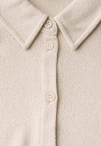 Krämfärgad stickad cardigan med textur, som har en spetsig krage och stängs med tre knappar med präglade detaljer. Mjuk material med ett löst vävt mönster.