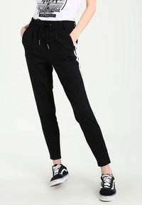 Svarta tapered-byxor med vita sidofickor, med dragsko i midjan och fickor, i kombination med svarta sneakers.