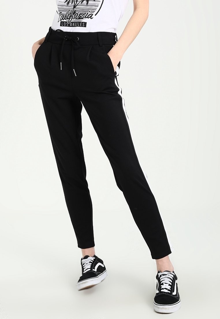 Svarta tapered-byxor med vita sidofickor, med dragsko i midjan och fickor, i kombination med svarta sneakers.