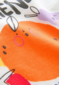 Colorful fabric featuring an orange circular shape with black dots and pink outlines, along with purple, yellow, and red accents. Textured surface.