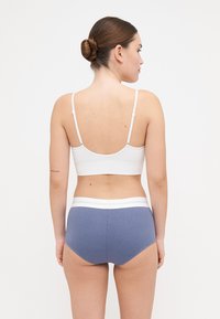Hvit ribbestrikket bralette med justerbare stropper, kombinert med blå ribbestrikkede shorts med høy midje som har en hvit midjebånd. Glatt tekstur.