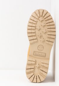 Timberland støvle sål i tan gummi, med dybe dækmønstre med krydsformer og et cirkulært logo i midten.