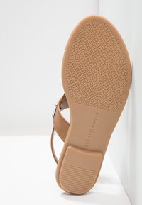 Semelle d'une sandale Tommy Hilfiger couleur bronzée avec une accroche avant texturée et un talon lisse, sangles et boucle partiellement visibles sur fond blanc.