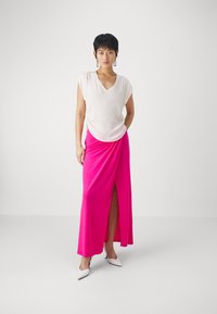 Hvit v-hals bluse med korte ermer, parret med et langt, lyst rosa skjørt med en frontslitt. Brukt med hvite hæler.