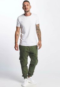 Biała koszulka i zielone spodnie cargo z kieszeniami, w połączeniu z białymi sneakerami; strój ma luźny krój i prosty design.