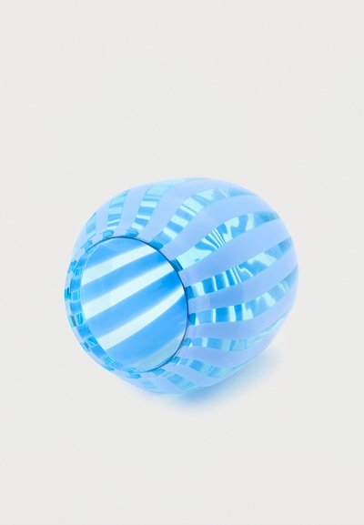 Μπλε ποτήρι από γυαλί με εναλλασσόμενες διάφανες και αδιαφανείς σπειροειδείς ρίγες, τοποθετημένο στο πλάι πάνω σε λευκό φόντο.