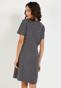 Vestido gris de manga corta con un respaldo estampado y un frente liso, que presenta un diseño geométrico sutil y un cuello redondo con un cierre en la parte posterior.
