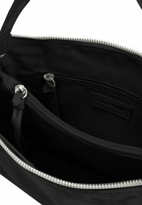 Interno di una borsa a mano di tessuto nero con un comparto con zip, cerniera argento e un piccolo etichetta cucita all'interno. Texture liscia senza motivi.