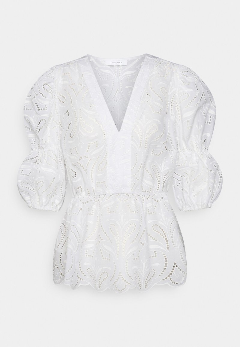 Blouse blanche en dentelle œillet avec manches trois-quarts bouffantes, décolleté en V profond, taille cintrée et ourlet festonné.
