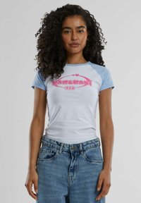 Camiseta de manga raglán en blanco y azul claro, con un logo gráfico en rosa en el centro. Material de algodón con una textura suave.