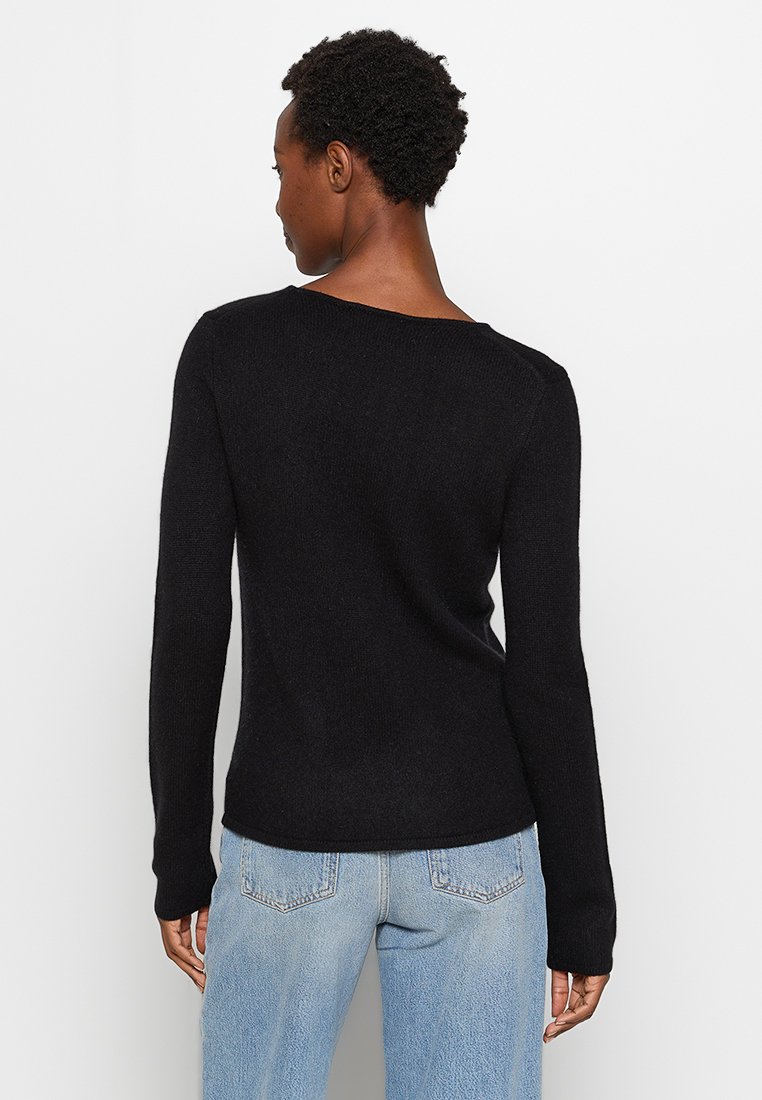 Schwarzer Pullover mit langen Ärmeln und strukturierter Oberfläche sowie einem weiten Ausschnitt, kombiniert mit hellblauen Jeans mit Gesäßtaschen.