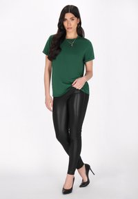 Grön kortärmad t-shirt med avslappnad passform, tillsammans med åtsittande svarta läderleggings och svarta högklackade skor. Enkelt design.