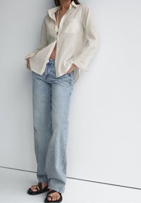 Lys beige button-up skjorte med en brystlomme, parret med lyseblå højtaljede jeans og sorte strop sandaler.