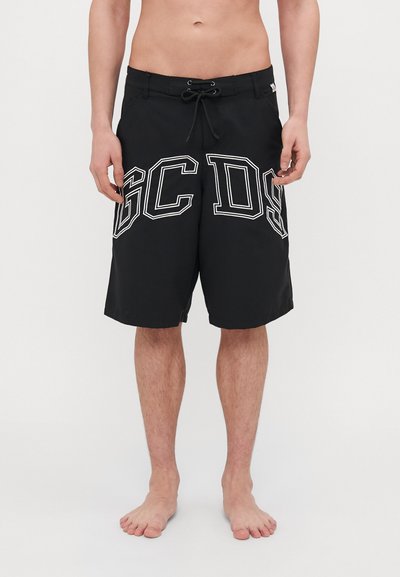 Schwarze Badehosen mit elastischem Bund und Kordelzug, großen weißen "GC DS" Buchstaben an jedem Bein und glatter Textur.