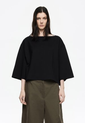 Top negro de gran tamaño hecho de algodón, con mangas anchas y dobladillo recto. Se combina con pantalones holgados de color verde oliva. Diseño simple y minimalista.