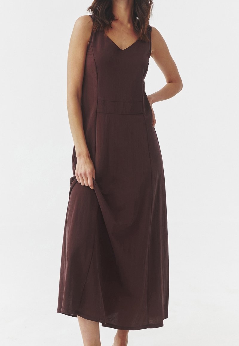 Robe bordeaux sans manches avec un col en V, une coupe mi-longue, un tissu texturé et un corsage ajusté avec des poches latérales.
