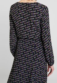 Abito nero con un motivo a ripetizione del logo "TOMMY JEANS" in testo multicolore, maniche lunghe, vestibilità ampia e texture del tessuto liscia.