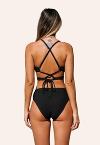 Černý žebrovaný bikini s křížovými ramínky a zavazovacím detailem. Vysoký pas kalhotek. Hladká textura, minimalistický styl.
