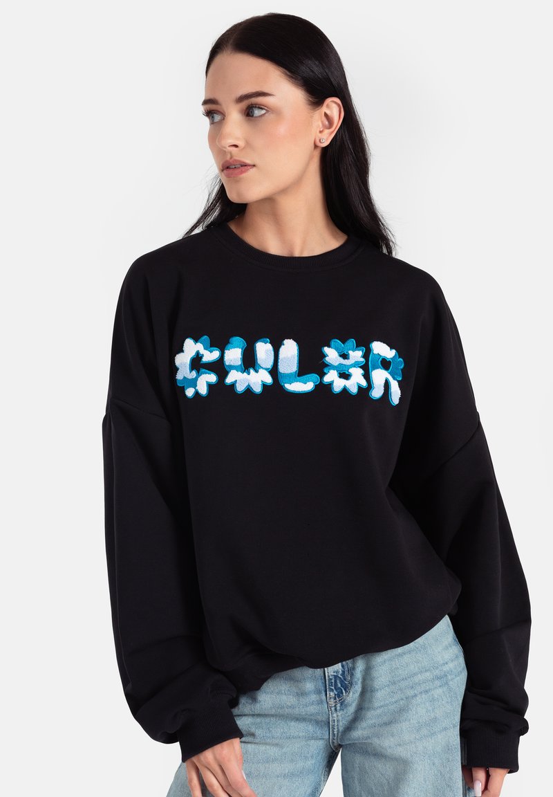 Czarna bluza z oversize'owym fasonem, teksturowana tkanina. Ozdobiona kolorowym, abstrakcyjnym wzorem kwiatowym w odcieniach niebieskiego i białego na przodzie.