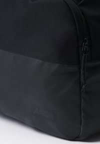 Schwarzer Stoff-Rucksack mit einem strukturierten oberen Bereich und einem glatten unteren Bereich. Verfügt über einen Reißverschluss und ein bedrucktes Logo-Patch.