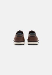 Zapatos de piel marrón con diseño redondeado, acento de talón azul contrastante y suela crema. La vista trasera resalta los detalles de la costura.