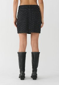 Mini falda de mezclilla negra con un patrón sutil, con bolsillos traseros y cintura ajustada. Combinada con botas de cuero negras hasta la rodilla.