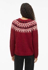 Pull en maille rouge avec un col rond, présentant un motif Fair Isle blanc et noir aux épaules. Design texturé et ample.