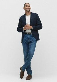 Marinblazer över en vit skjorta, kombinerad med blå jeans och bruna skor. Outfiten har en avslappnad men polerad look och en bälte.