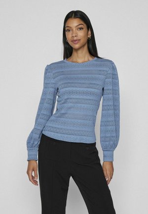 Hele sinine pikkade varrukatega pluus, millel on tekstiilne vertikaalne triip ja puffse varrukad. Omab ümmargust kaelust ja vormitud hem.