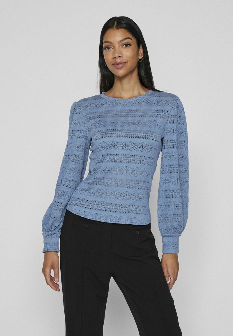 Světle modrá blůza s dlouhými rukávy, texturovanými vertikálními pruhy a nabíranými rukávy. Má kulatý výstřih a přiléhavý lem.